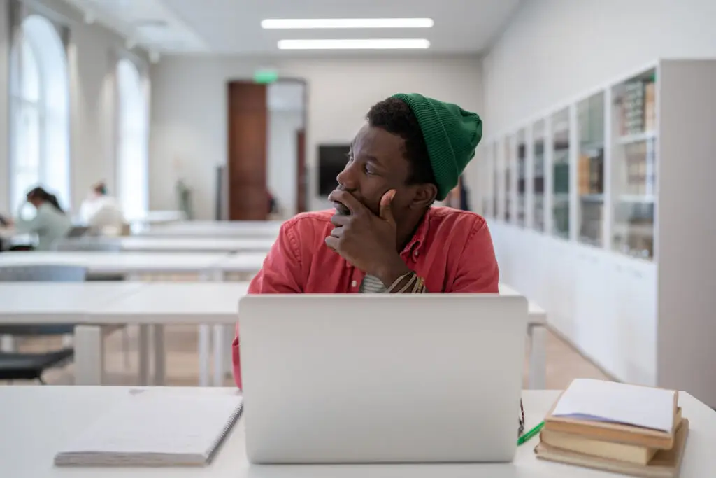 Procrastination concept. Thoughtful Black student man looking away while studying in library, pensive lost in thoughts African American guy learner disinterested in study looking into distance